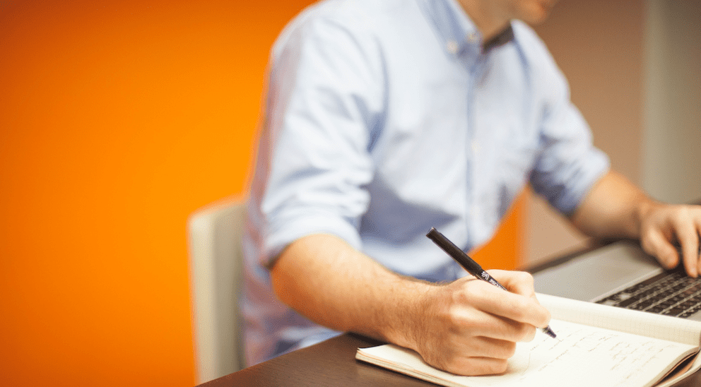 Man writing a brand story in a notebook and on a computer