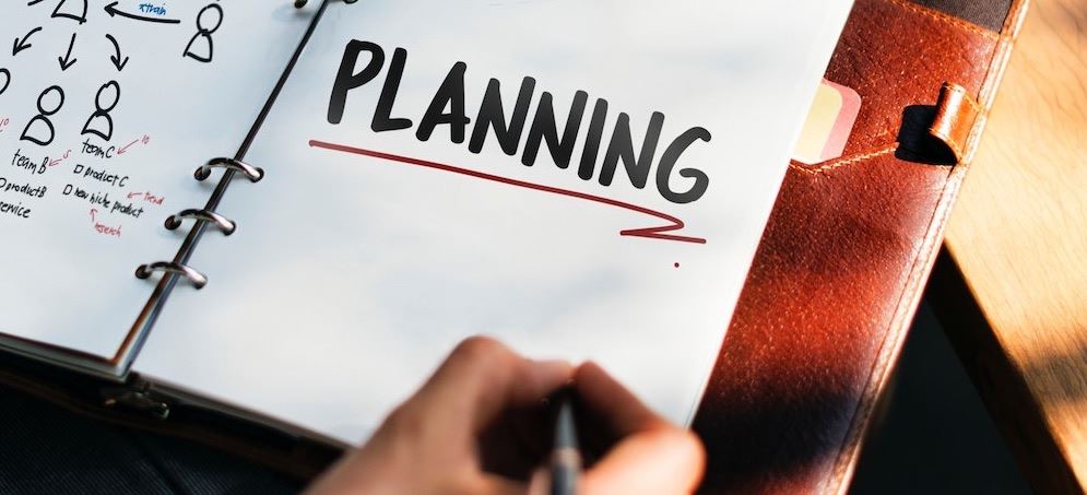 Person writing a plan in a notebook that says planning