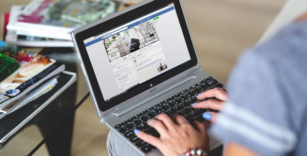 Person typing on a laptop on their lap looking at Facebook